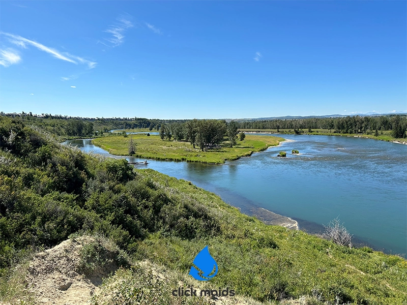 "Winding river through lush greenery under clear blue sky, with 'click maids' logo at bottom center."