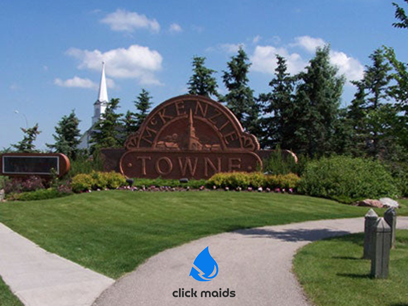 McKenzie Towne Calgary sign on grassy hill; white church steeple and blue sky background.