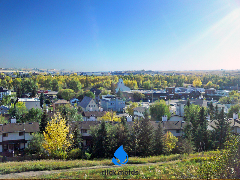 Sunny view of Cochrane Alberta with colorful trees, residential rooftops, and a clear blue sky